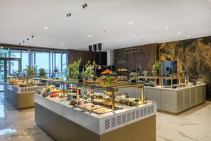 Zona de bufé con diferentes estaciones de comida y un amplio ventanal con vistas al exterior.