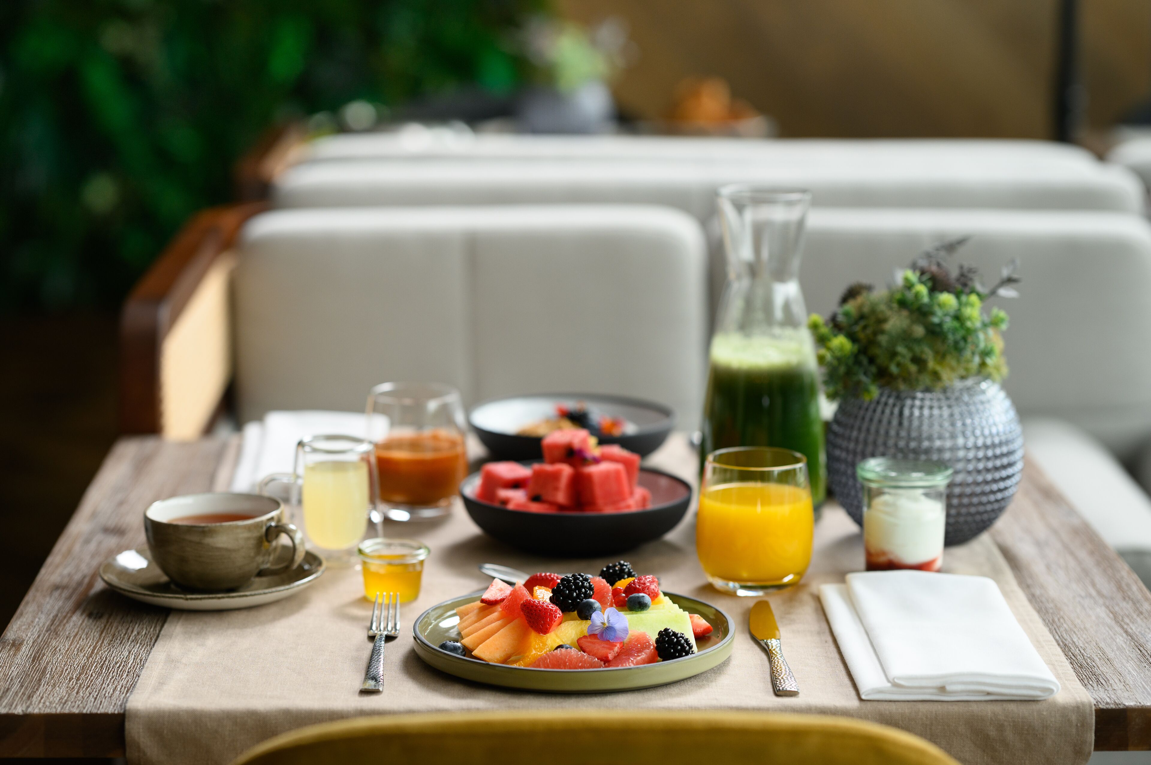 A breakfast table with various fruits, beverages, and a cup of tea.