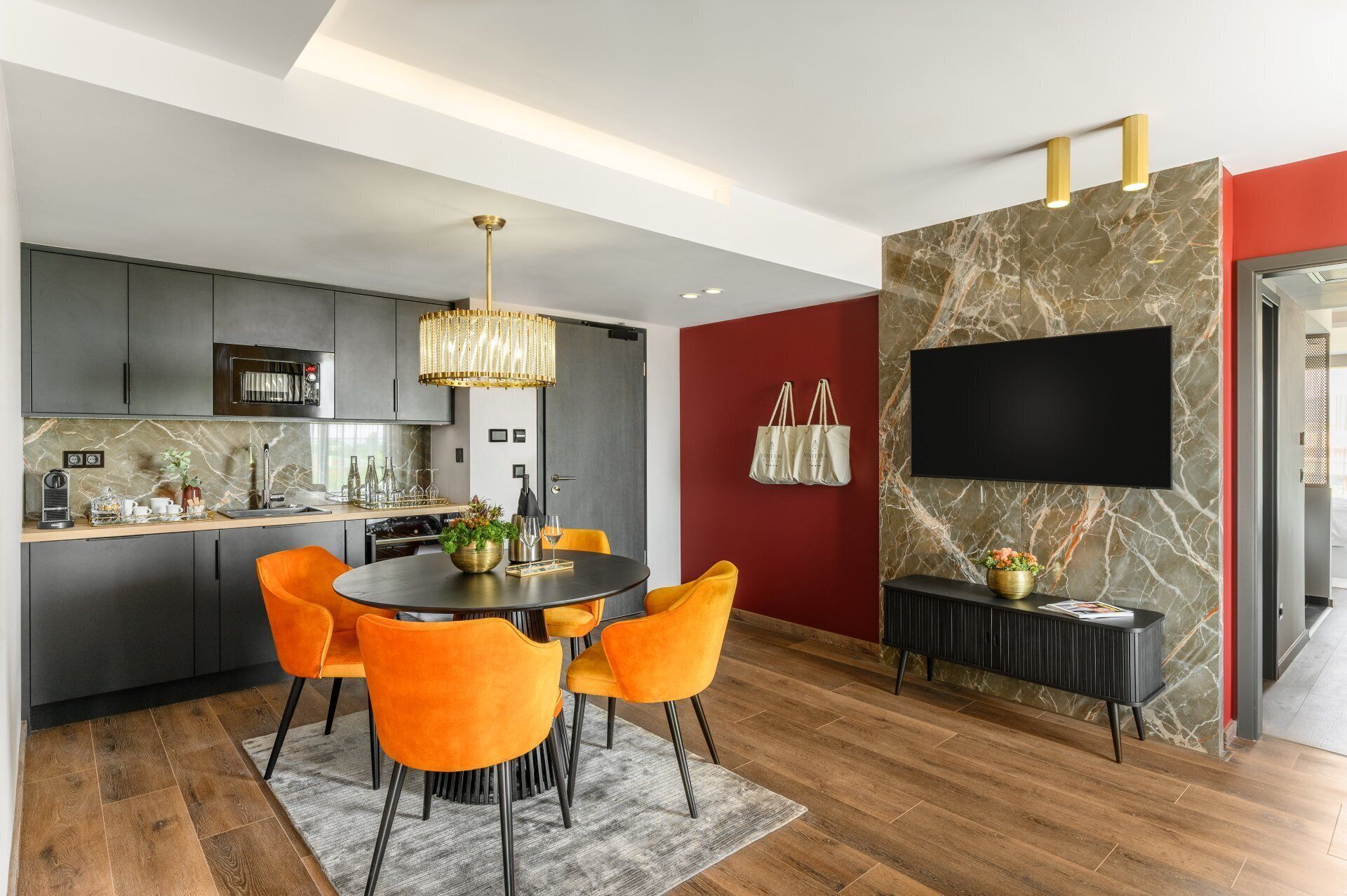Una cocina moderna con armarios oscuros, una isla central y una zona de comedor con sillas color naranja.