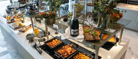 A buffet with various food items, a bottle of champagne, and decorative plants.