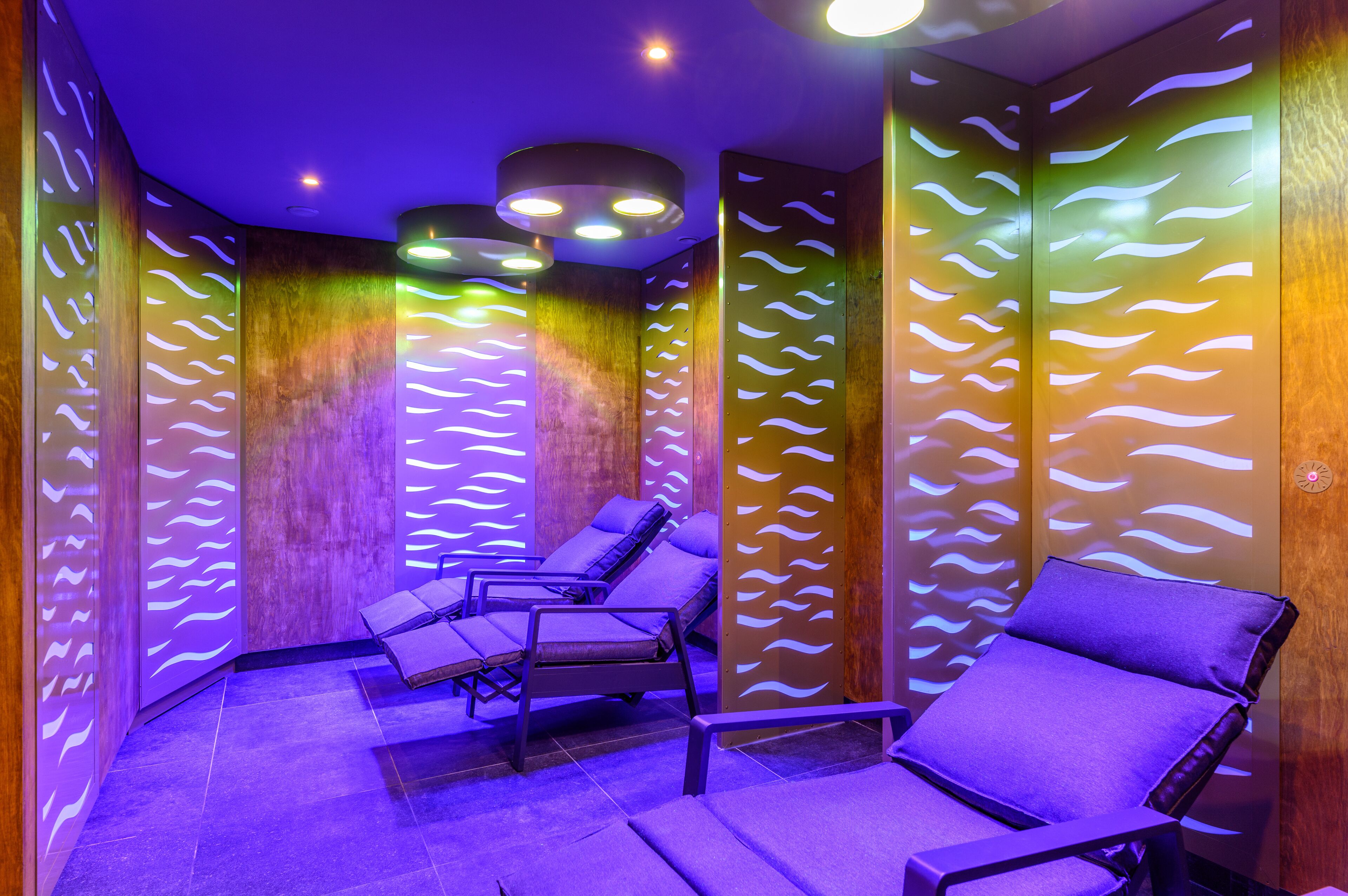 Un cuarto de spa con tres sillas reclinables, paneles de madera y luces en el techo.