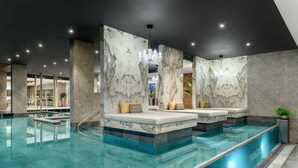 A modern indoor pool area with marble walls, seating, and a clear pool. - Hotel Vinifera Wine & Spa (Balatonfured)