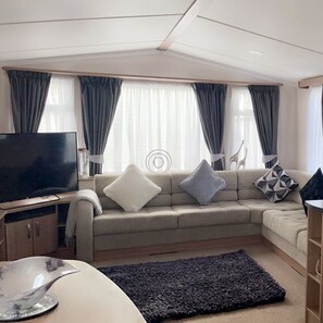 A modern living room with a sofa, a flat-screen TV, and a decorative bowl on a table. - Remarkable 3-bed Caravan, Direct Beach Access (Skegness)