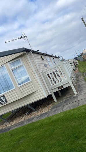 A mobile home with a satellite dish, a small porch, and a grassy yard. - Remarkable 3-bed Caravan, Direct Beach Access (Skegness)