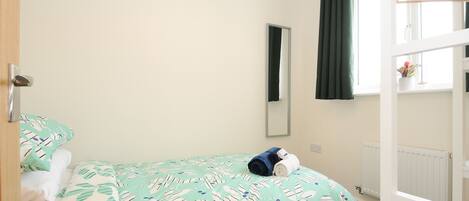 A bedroom with a bed, a window with curtains, a radiator, and a wooden wardrobe.