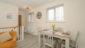 A dining area with a wooden table set for four, white chairs, and a clock on the wall. - Trewhiddle Retreat (St Austell)