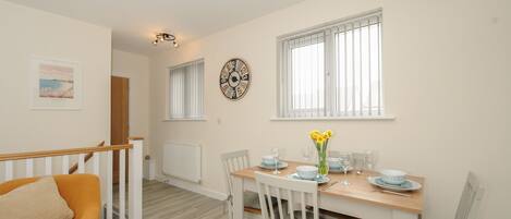 A dining area with a wooden table set for four, white chairs, and a clock on the wall.