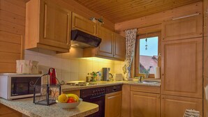 A kitchen with wooden cabinets, a microwave, a sink, and a window with a curtain. - Doppelhaushälfte in Hasselfelde (Hasselfelde)