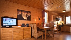A wooden interior with a television, a painting, a deer head, and a dining area.