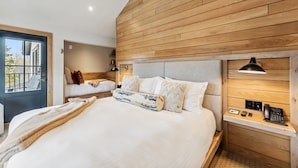 A modern hotel room with a large bed, a bedside table with a lamp, and a view of the outside. - The Carlin Lomax | Balcony views, family-friendly (Breckenridge)