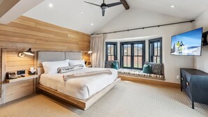 A modern bedroom with a large bed, wooden headboard, bedside tables, a ceiling fan, a window seat with cushions, and a TV mounted on the wall. - The Carlin Royal Tiger | Bunks, Views & Balcony (Breckenridge)