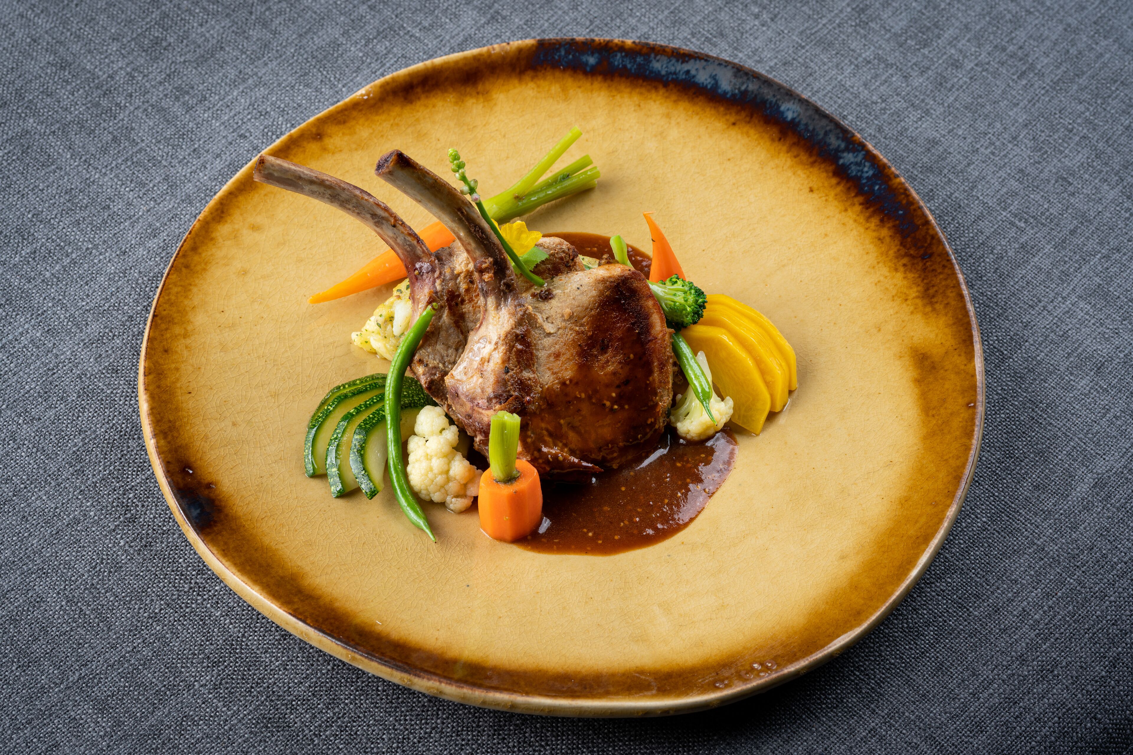 A plate of food with a lamb chop, vegetables, and sauce.