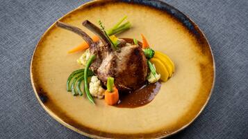 A plate of food with a lamb chop, vegetables, and sauce.