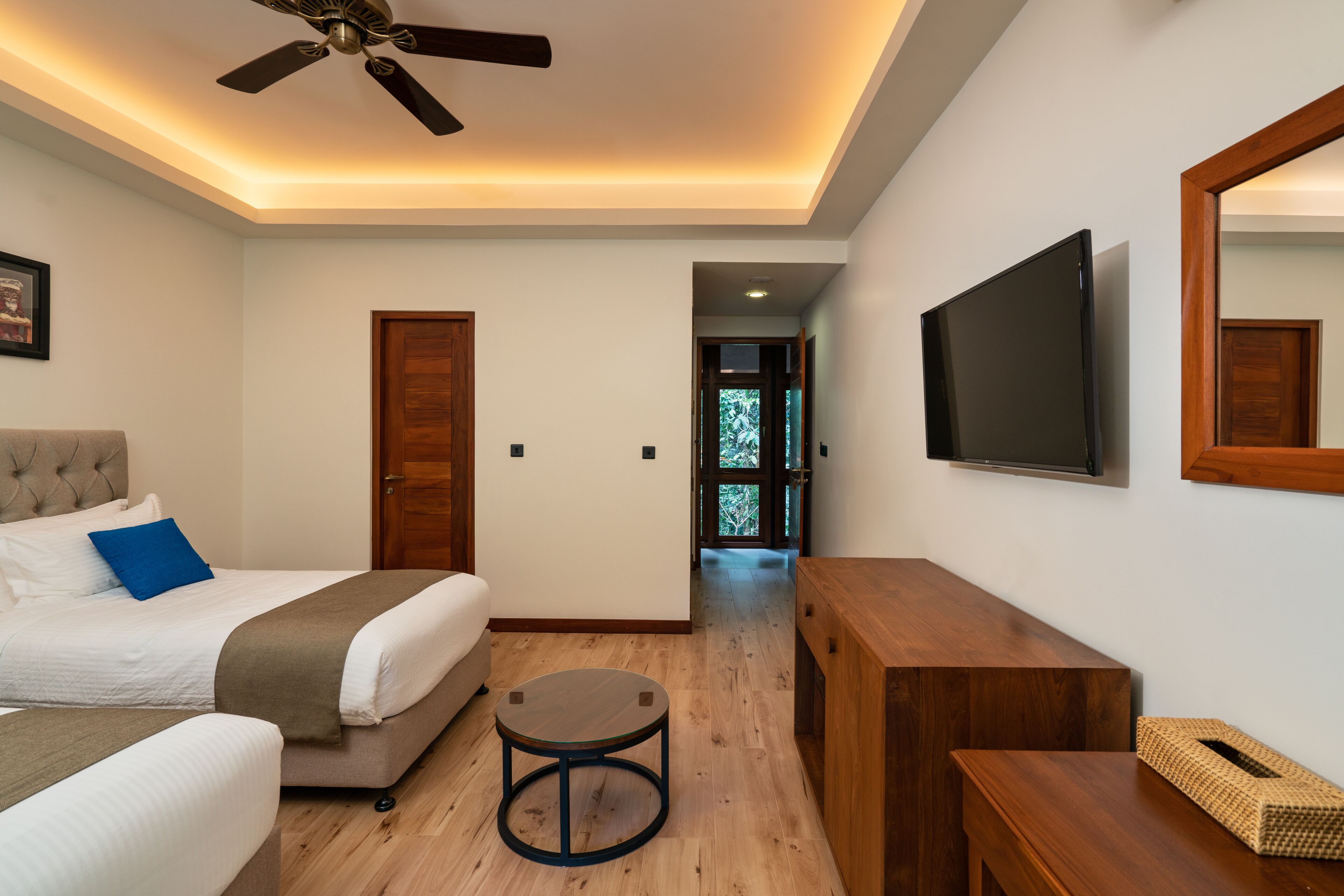 Habitación de hotel con cama, ventilador de techo, televisor y escritorio de madera.