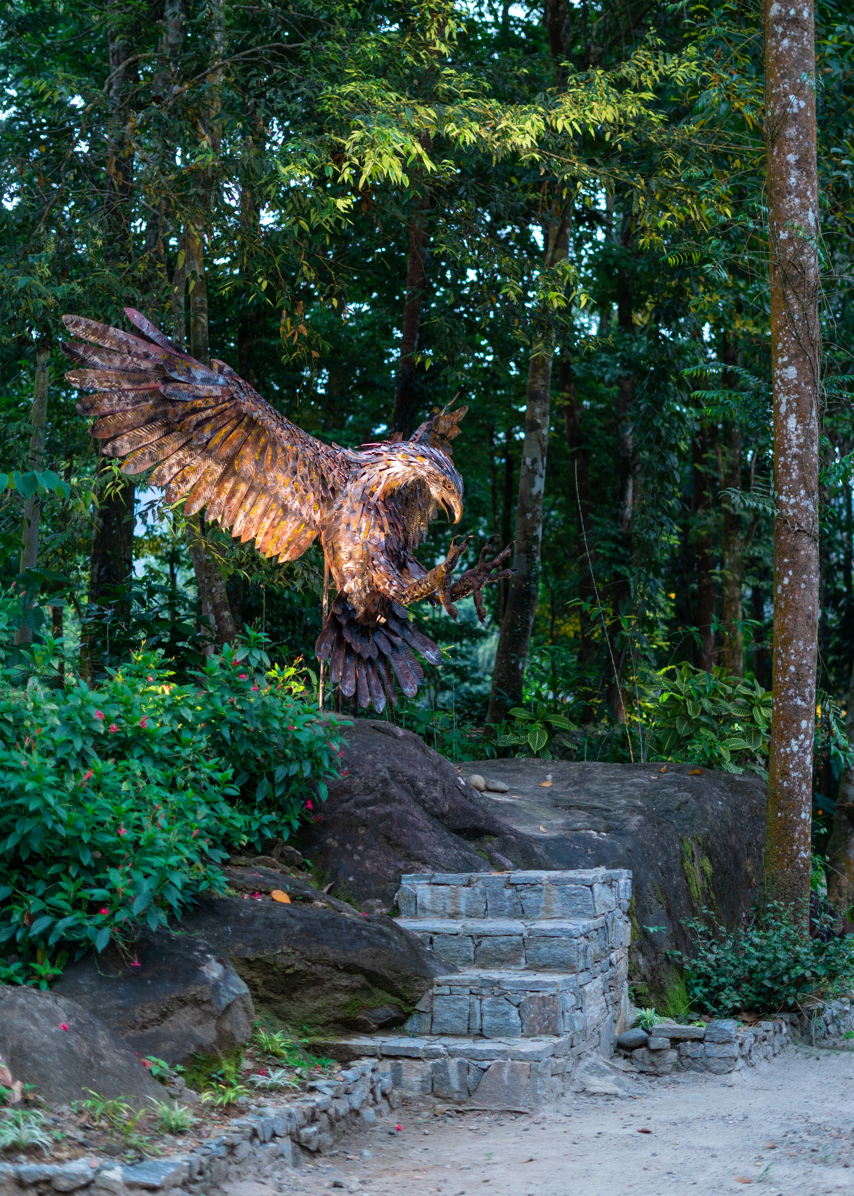 A large bird sculpture in a forested area with stone steps leading up to it.