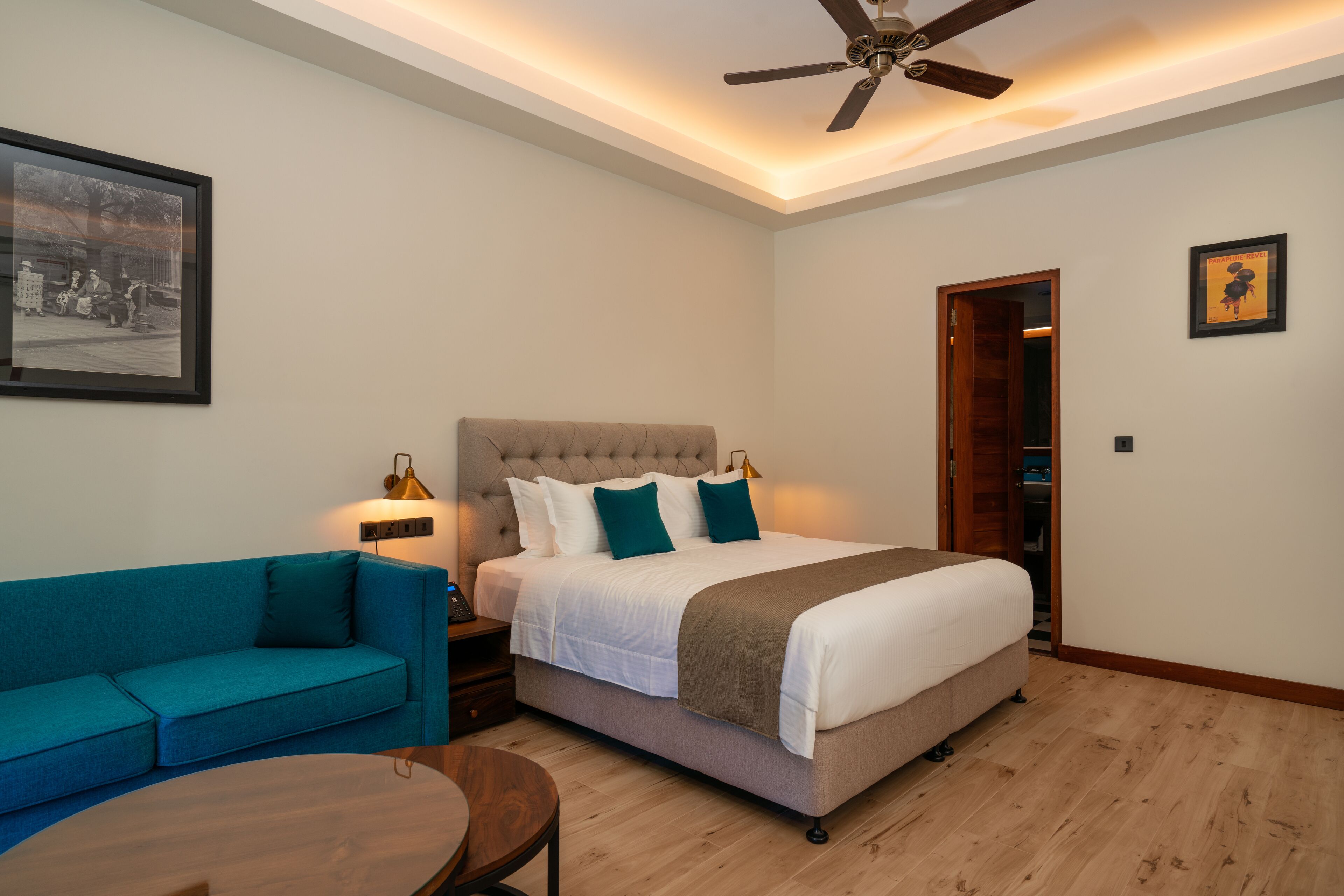 Un dormitorio moderno con cama, sofá azul, mesa de centro de madera y ventilador de techo.