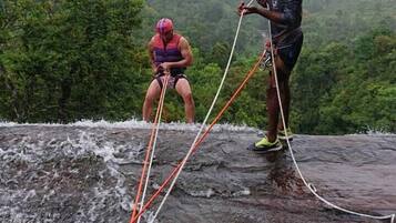 Two people rappelling on a wet rock surface with a forested mountain in the background.