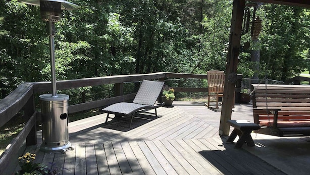Una terraza de madera con un calentador metálico, una silla acolchada y un banco.