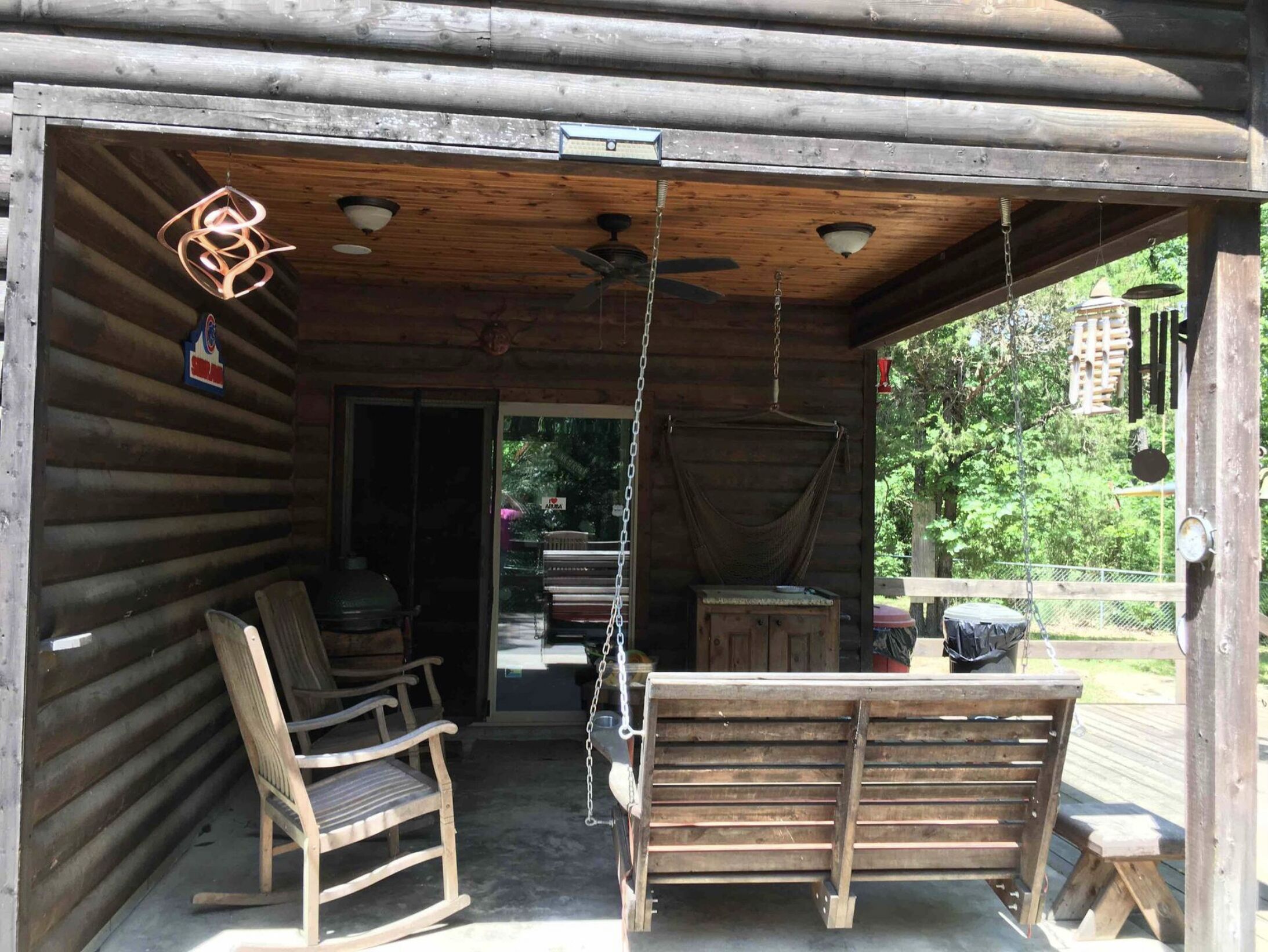 Une cabane en bois avec une véranda, une chaise berçante, un banc et un luminaire suspendu.