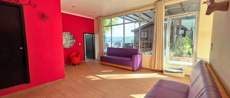 A room with a red wall, a purple sofa, and a large window with a view.