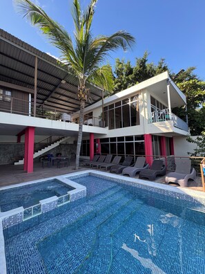 A two-story building with a swimming pool, outdoor seating, and a staircase.