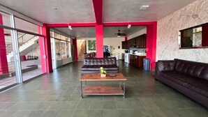 A spacious living area with a leather sofa, a wooden coffee table, and a kitchen in the background. - Quinta Sunset - Coatepeque Lake (El Congo)