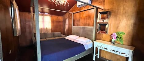 Ein Himmelbett mit dunkelblauer Bettdecke, ein weißer Nachttisch mit Blumenvase und eine Holzwand mit Spiegel.
