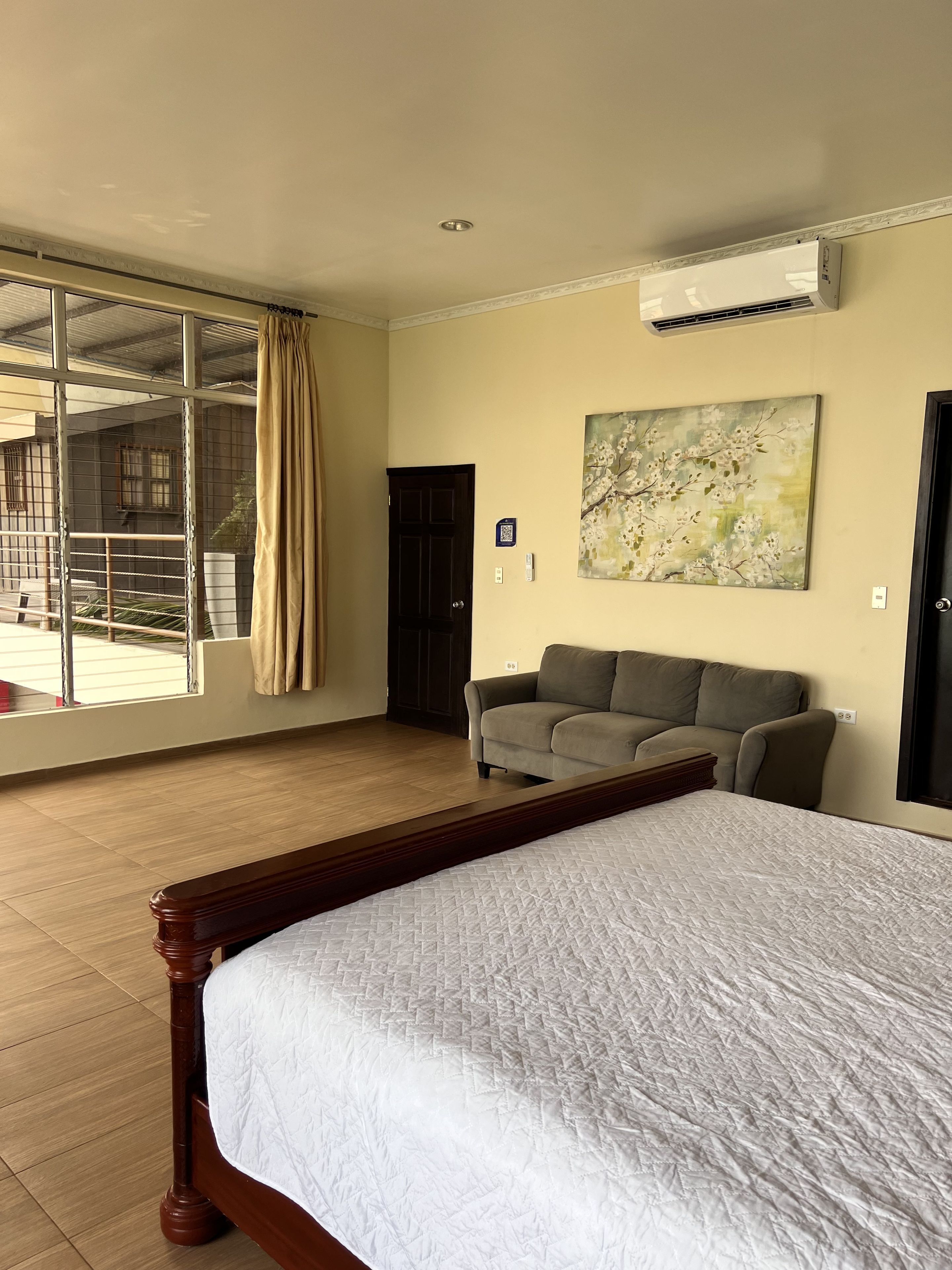 A hotel room with a large bed, a sofa, a painting, and a view of a building outside.
