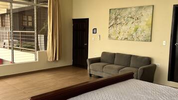 A hotel room with a large bed, a sofa, a painting, and a view of a building outside.