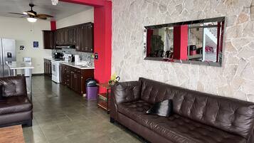 A living room with a brown leather sofa, a dining area with a white table, and a kitchen with dark cabinets.