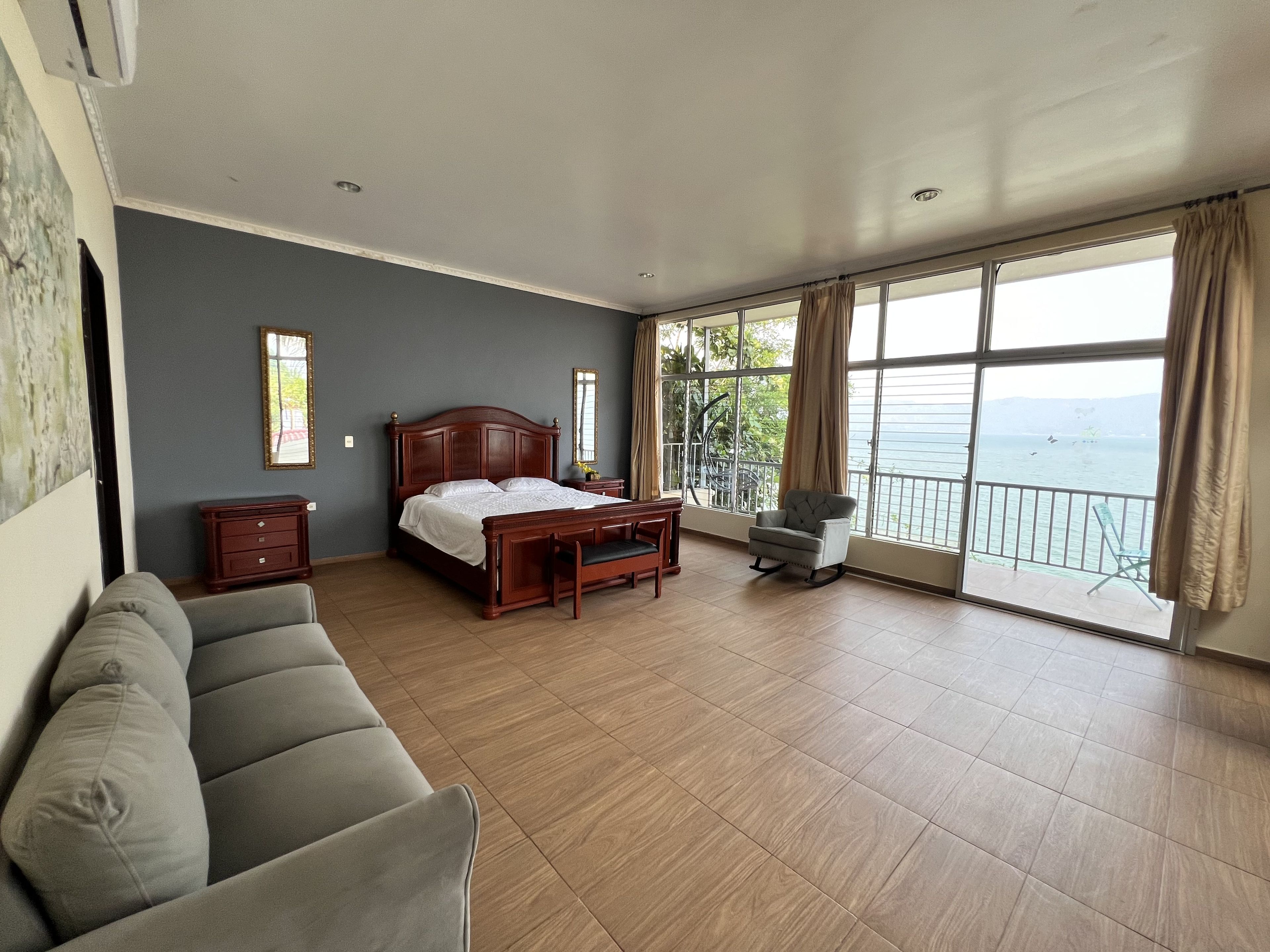 Un dormitorio con cama, sofá, silla y ventana grande con vista al mar.