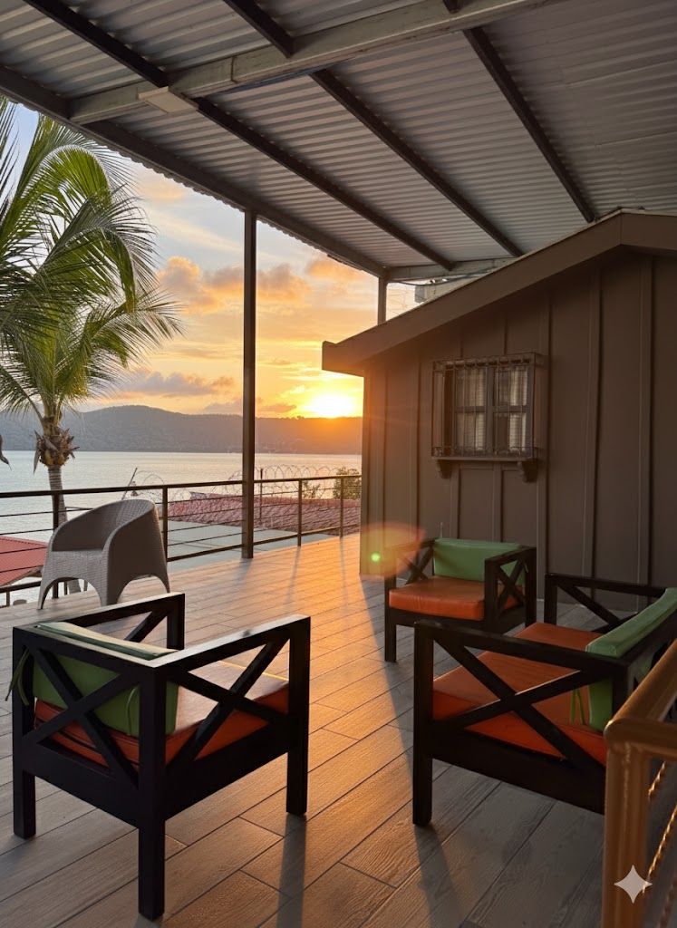 A covered outdoor seating area with chairs and a table, overlooking a body of water and a sunset.