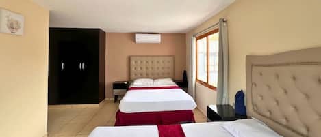 A hotel room with two beds, a wardrobe, a window with curtains, and a ceiling light.