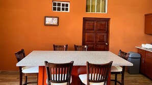 A dining area with a rectangular table, six chairs, a wooden door, and a window with curtains. - Quinta Sunrise - Coatepeque Lake (Planes de la Laguna)