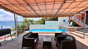 An outdoor seating area with a pool, overlooking a body of water and mountains. - Quinta Sunrise - Coatepeque Lake (Planes de la Laguna)