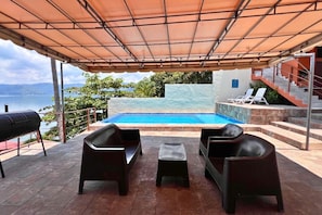 Uma área de estar externa com piscina, com vista para um corpo de água e montanhas.