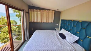 A bedroom with a bed, a headboard, a window with curtains, and a view of greenery. - Quinta Sunrise - Coatepeque Lake (Planes de la Laguna)
