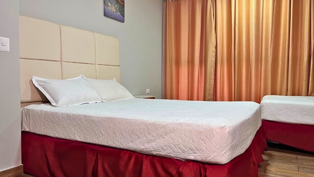 A hotel room with a bed, a nightstand, a red skirted bed base, and a window with curtains. - Quinta Sunrise - Coatepeque Lake (Planes de la Laguna)