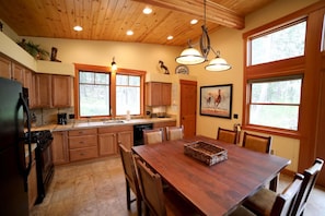 A kitchen with wooden cabinets, a dining table, and large windows. - Horseman’s Hideaway 2 bedroom cabin - dogs welcome (Winthrop)