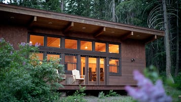Una cabaña de madera con ventanas amplias, una terraza y una silla.