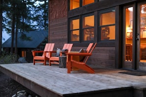 A wooden deck with two orange Adirondack chairs, a small table, and a tree stump.