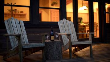 Dos sillas Adirondack de madera en una terraza de madera, con una botella y vasos sobre un tocón.
