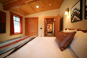 A bedroom with a wooden ceiling, a bed with a striped blanket, a brown pillow, and a wall-mounted light fixture.