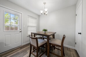 Ein Essbereich mit einem Holztisch, vier Stühlen, einer Chandelierleuchtre, einem Blumentopf und einer Tür mit Fenster.