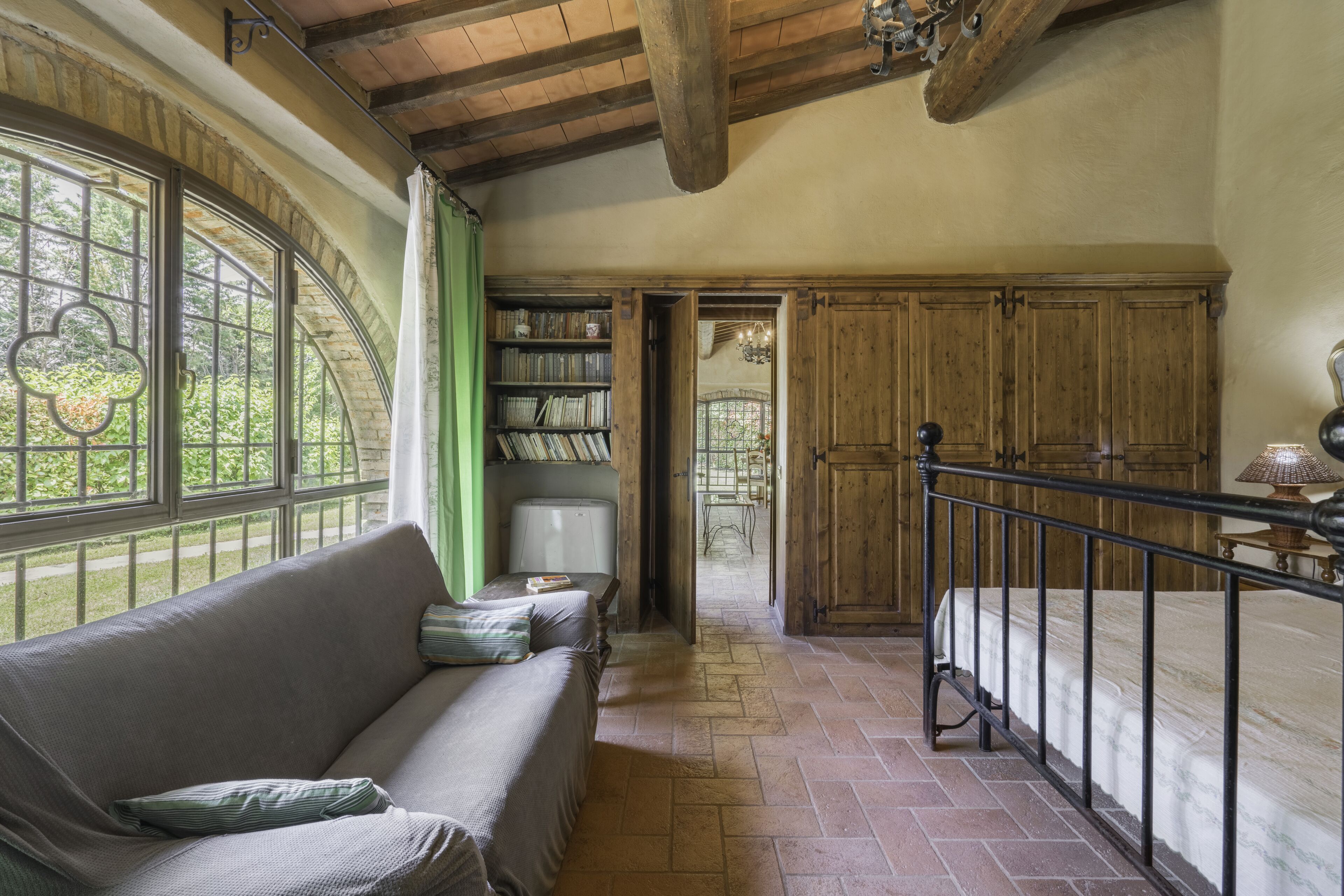 Une pièce chaleureuse avec un plafond en bois, un canapé vert, un lit avec un cadre en métal et une bibliothèque remplie de livres.