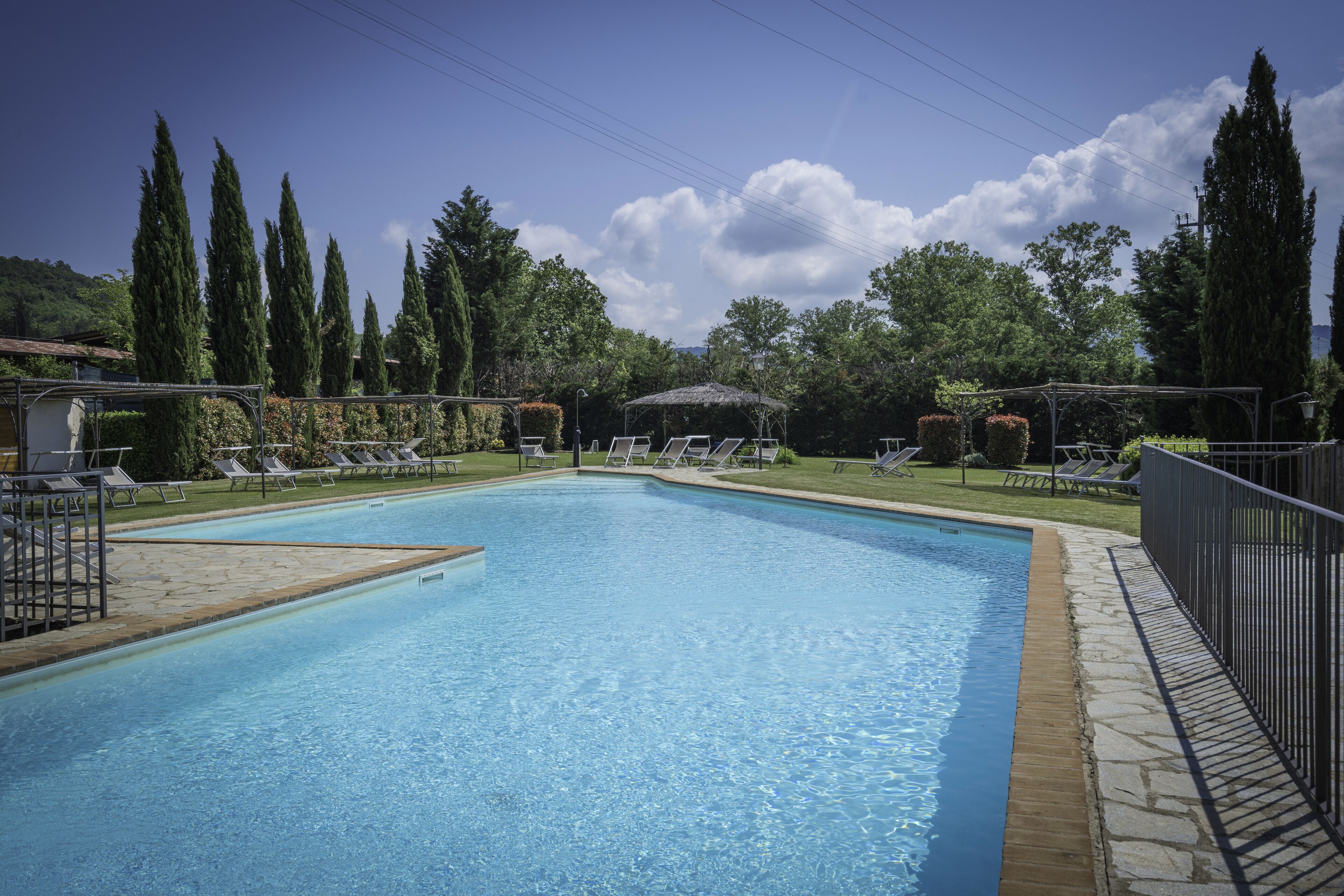 A rectangular swimming pool with clear blue water, surrounded by lounge chairs and a covered seating area.