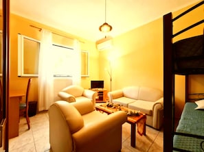 A room with a sofa, a smaller chair, a table, a TV, a radiator, and a bunk bed.