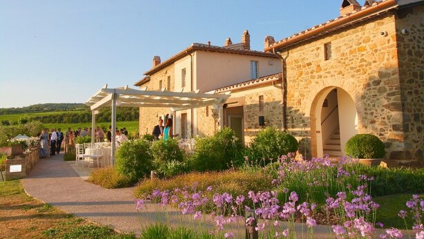 Un bâtiment en pierre doté d’un espace extérieur couvert et d’un jardin agrémenté de fleurs violettes.