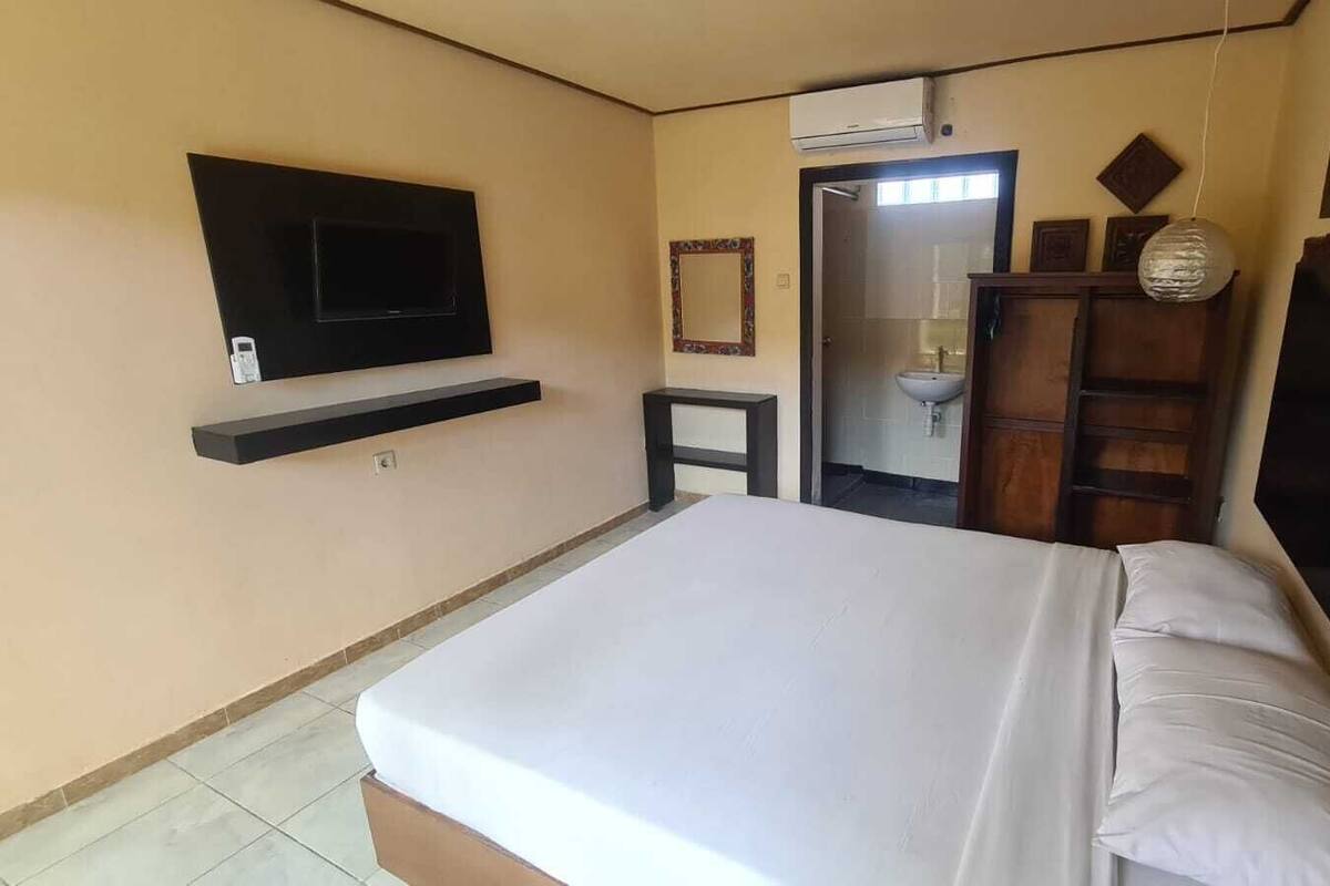 A bedroom with a bed, a TV mounted on the wall, a small bedside table, and a wardrobe.