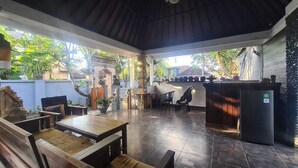 An outdoor patio with wooden furniture, a refrigerator, and a stone statue.